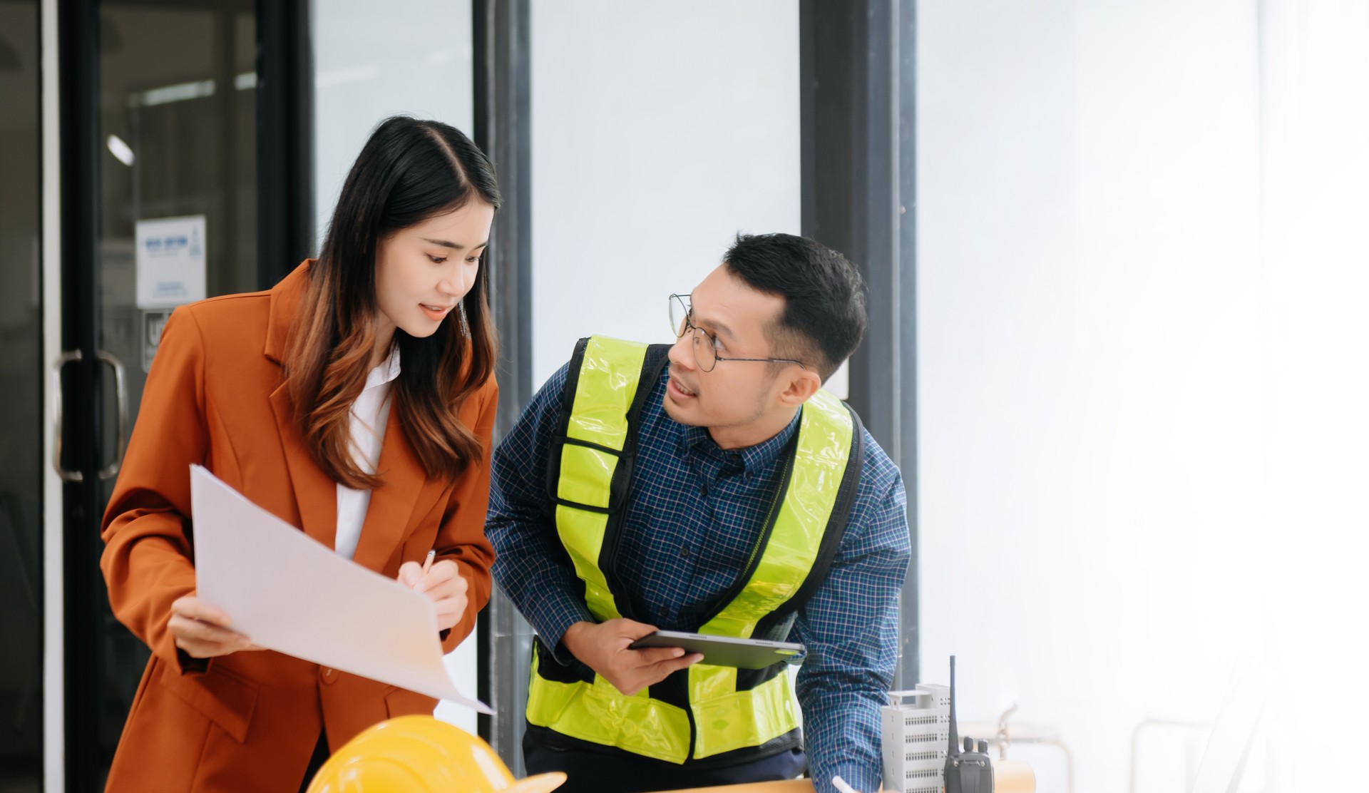 Two colleagues discussing data working and tablet, laptop with on architectural project at construction site at desk in office